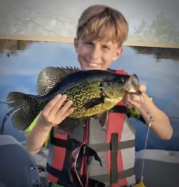 Small boy holding up a Florida black crappie he caught on rod/reel from a boat on a lake in central Florida.