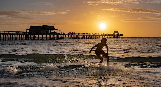 Surfer beside Naples Fishing Pier at sunset in Florida.